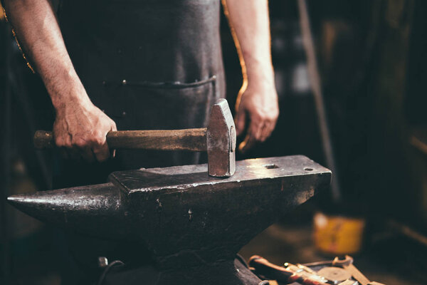 Close-up of blacksmith manually forging the molten metal on the anvil in smithy workshop. Blacksmith working metal with hammer in the forge