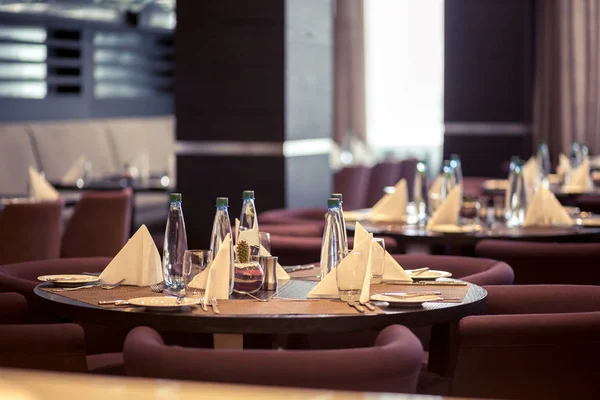 Salón semi-iluminado en estilo loft en un restaurante mexicano con cocina abierta en el fondo. Delante de la cocina hay mesas de madera con sillas y sofás multicolores. En los sofás — Foto de Stock