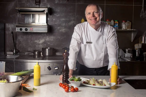 Portret van een glimlachende mannelijke chef-kok met gekookt voedsel staan in de keuken — Stockfoto