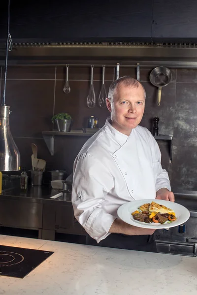 Portret van een glimlachende mannelijke chef-kok met gekookt voedsel staan in de keuken — Stockfoto