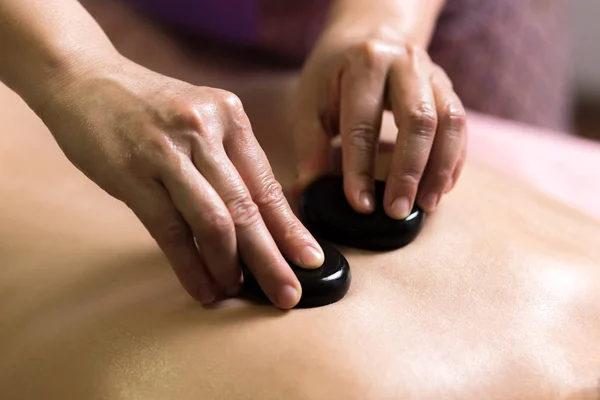 Beskuren bild av massageterapeut sätta spa stenar på baksidan av flicka liggande på en massagebänk — Stockfoto