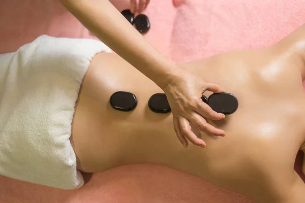 Mujer recibiendo masaje de piedra caliente en el salón de spa. Concepto de tratamiento de belleza. — Foto de Stock