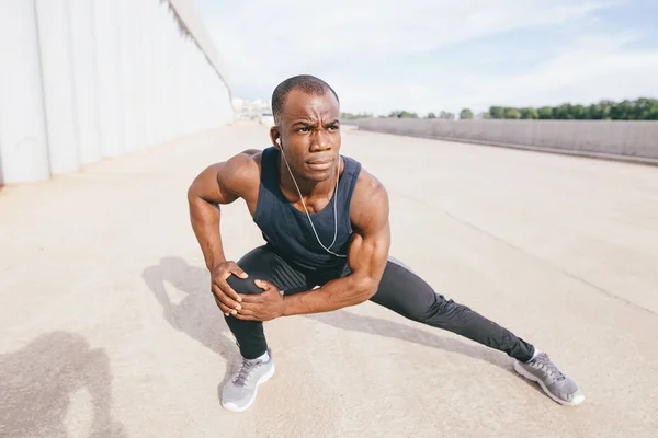 Manliga löpare i svart sportkläder stretching benen innan morgon träning — Stockfoto