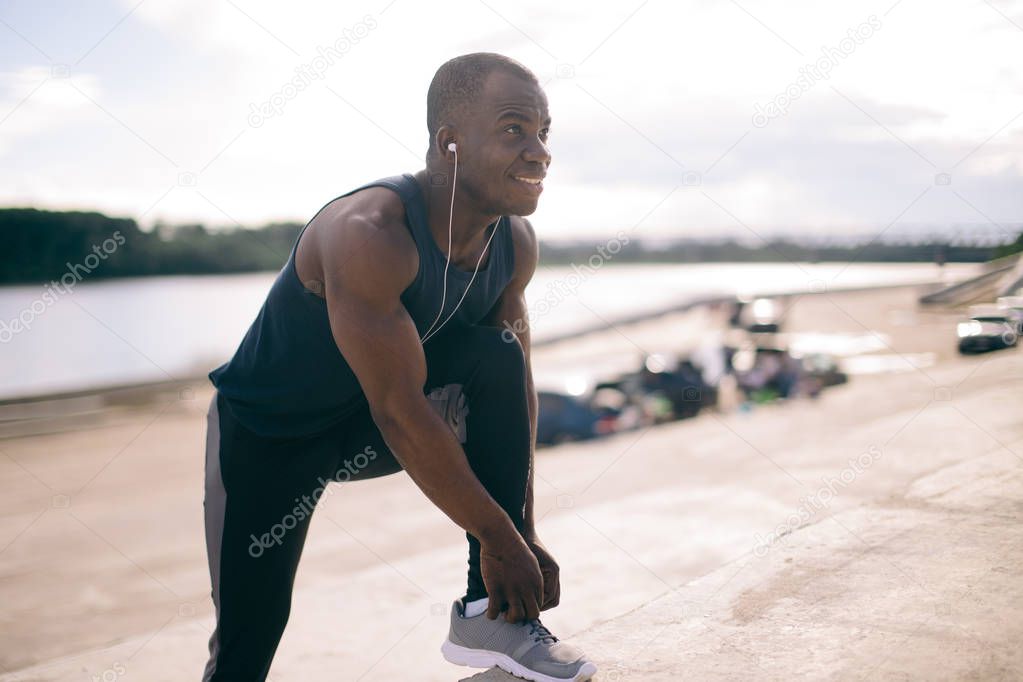 african male runner tying his shoe on steps