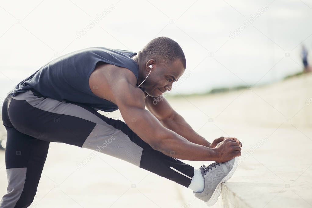 male runner in black sportswear stretching legs before doing morning workout.