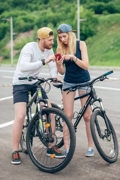 Jeune couple joyeux à vélo regardant dans le téléphone intelligent, télécharger des photos prises — Photo