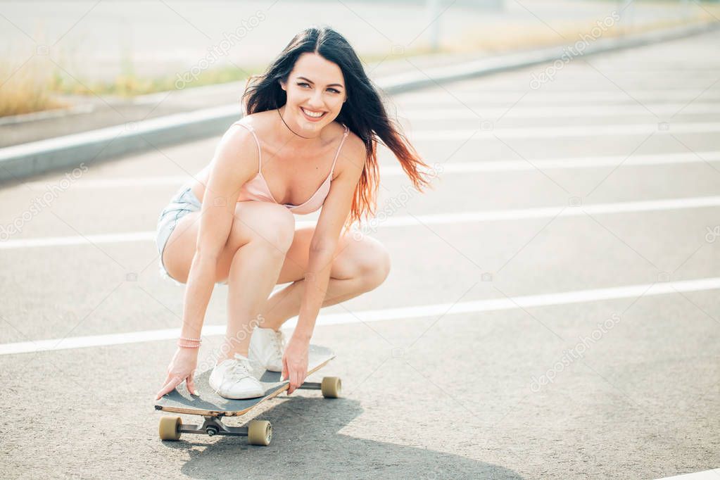 Beautiful young girl sits and ride on longboard in sunny weather