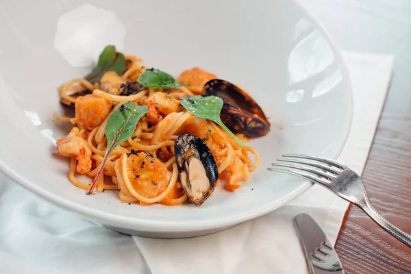 Deniz ürünleri makarna midye ve ahşap masa üzerinde beyaz tabak içinde fesleğen ile.