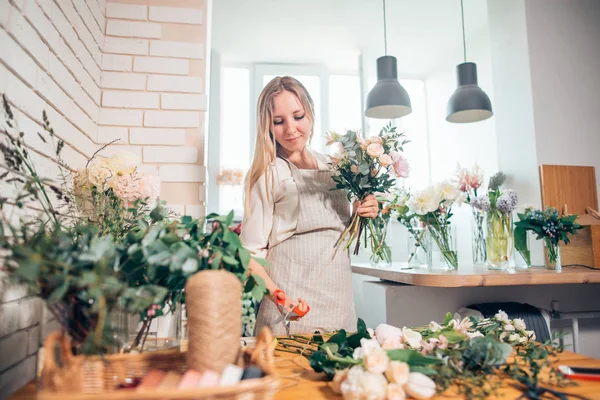 Sonriente encantadora florista joven que arregla las plantas en la tienda de flores — Foto de Stock