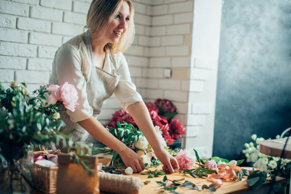 Sonriente encantadora florista joven que arregla las plantas en la tienda de flores — Foto de Stock