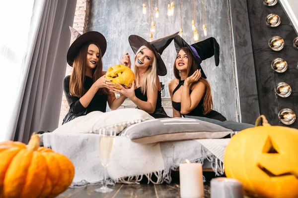 Three adult women carve Halloween pumpkins while laughing and having a party