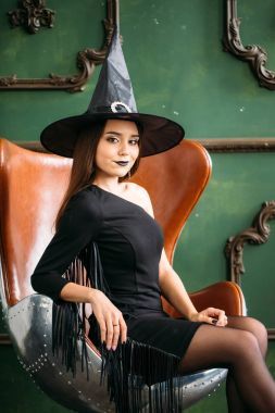 Mutlu Gotik genç kadın cadı halloween kılık koltuğa oturan şapkalı