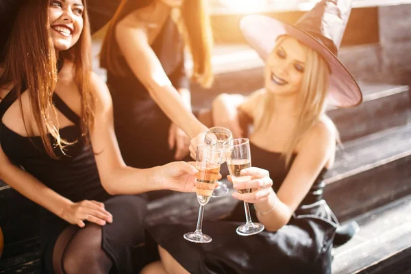 Tre ragazze si siedono e battono i bicchieri con champagne — Foto Stock