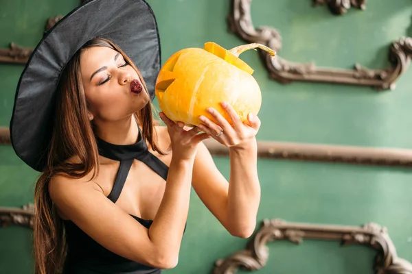 Halloween. Sexy dame in het rood met grote pompoen op haar handen — Stockfoto