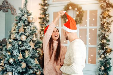 Fotoğraf genç çiftin Noel ağacında kucaklaşmalarını gösteriyor.