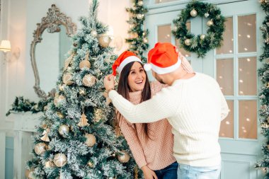 Fotoğraf genç çiftin Noel ağacında kucaklaşmalarını gösteriyor.