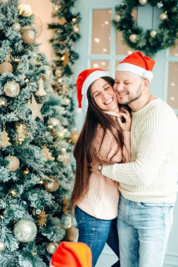 Fotoğraf genç çiftin Noel ağacında kucaklaşmalarını gösteriyor.