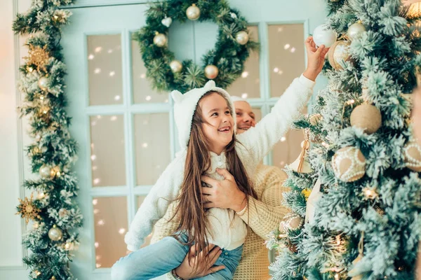 Дівчина допомагає батькові прикрашати ялинку, тримаючи деякі різдвяні сукні — стокове фото
