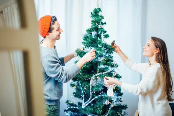 Pareja feliz joven decorando un árbol de Navidad. Luz natural, enfoque selectivo — Foto de Stock