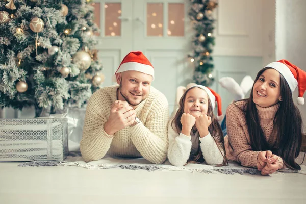 Οικογένεια στο Santa Χριστούγεννα καπέλα ξαπλωμένος στο κρεβάτι. Ο πατέρας η μητέρα και το μωρό έχουν τη διασκέδαση — Φωτογραφία Αρχείου