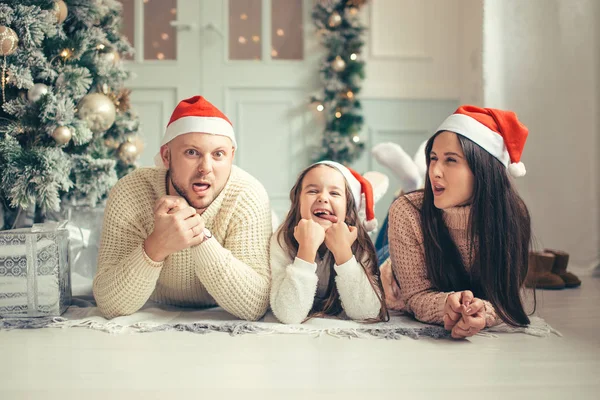 Οικογένεια στο Santa Χριστούγεννα καπέλα ξαπλωμένος στο κρεβάτι. Ο πατέρας η μητέρα και το μωρό έχουν τη διασκέδαση — Φωτογραφία Αρχείου