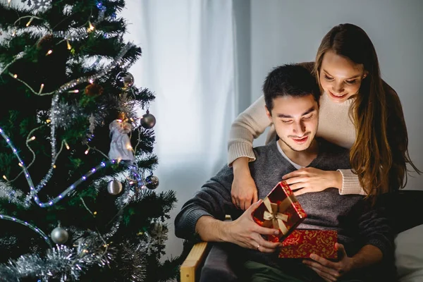 Mladá žena s manželem při pohledu na vánoční dárek — Stock fotografie