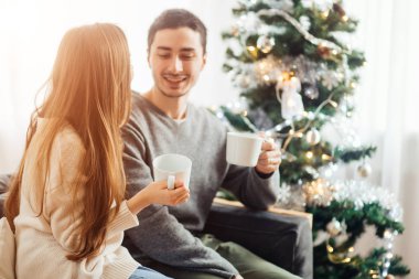 Erkek ve kadın sıcak içecek beyaz Noel ağacı daha önce oturan bardak tutun