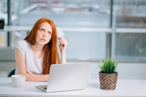Pensando mulher de negócios sentada à mesa com laptop, segurando cartão de crédito vazio — Fotografia de Stock