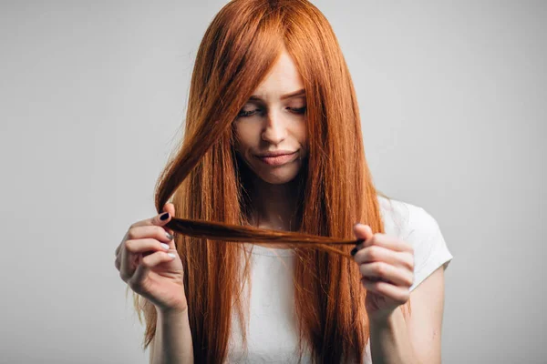 Triste rossa ragazza guardando i suoi capelli danneggiati — Foto Stock
