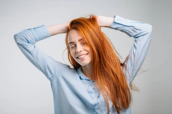 Młoda ładna ruda dziewczyna z piegami patrząc na aparat uśmiechnięty dotykające włosy — Zdjęcie stockowe
