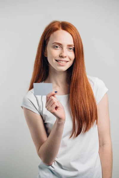 Pelirroja sosteniendo tarjeta de crédito y sonriendo sobre fondo blanco . — Foto de Stock