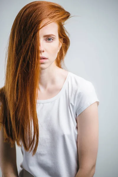Jovem menina ruiva bonita com sardas olhando para a câmera sorrindo tocando o cabelo — Fotografia de Stock