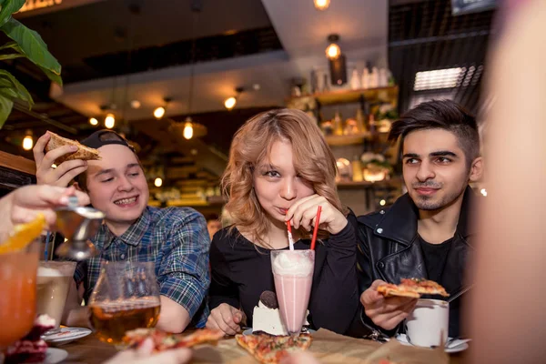 Jonge vrouw drinken milkshake zittend met vrienden bij café — Stockfoto