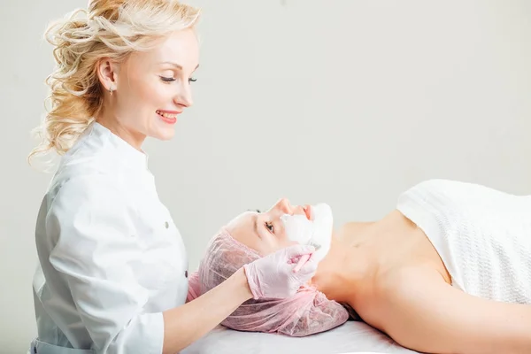 Mujer recibiendo cuidado facial por esteticista en el salón de spa, vista lateral, primer plano . — Foto de Stock
