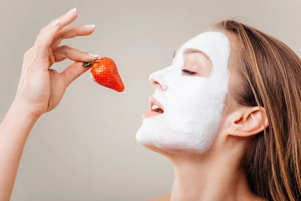 Wanita makan stroberi. Wanita cantik muda dengan masker wajah dan strawberry — Stok Foto