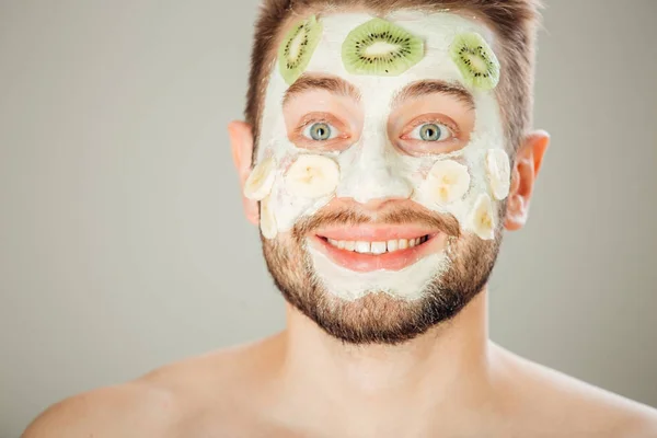 Homme avec masque cosmétique sur le visage, fond gris — Photo