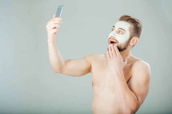 Jeune et bel homme avec masque purifiant sur son visage faisant selfie — Photo
