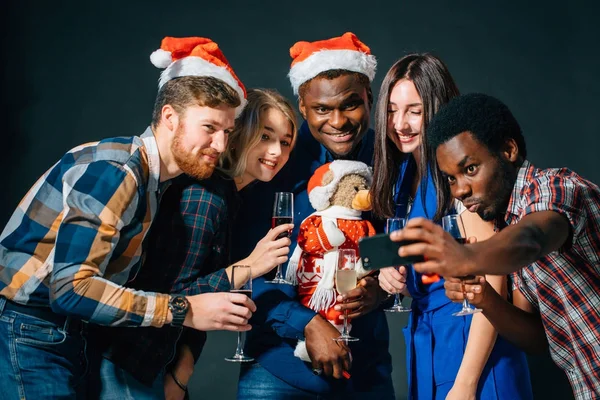 Chicas y chicos en sombreros de Santa haciendo selfie en la fiesta. Navidad, concepto de año nuevo — Foto de Stock