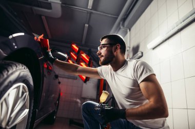 Araba temizliği. Adam mikrofiberi elinde tutuyor ve arabayı cilalıyor.