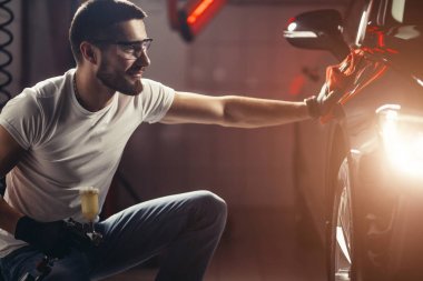 Araba temizliği. Adam mikrofiberi elinde tutuyor ve arabayı cilalıyor.