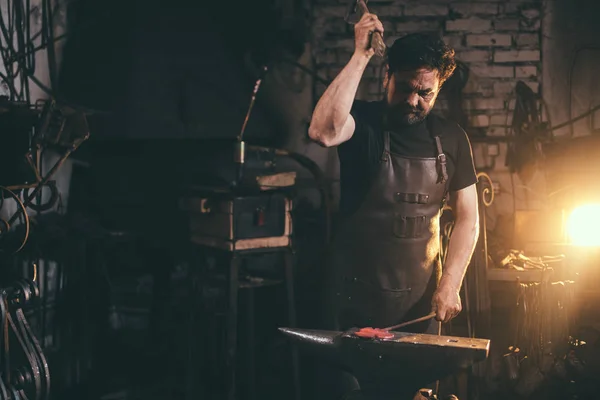 Ferreiro trabalhando metal com martelo na bigorna na forja — Fotografia de Stock