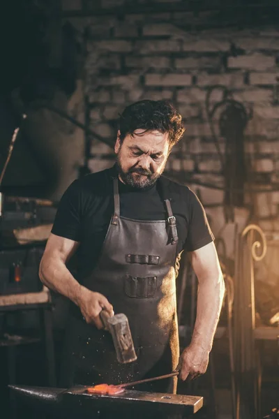 Herrero trabajando metal con martillo en yunque en la forja — Foto de Stock