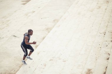 Afrikalı siyah sporcu stadyum tribünlerinde enerjisiyle yukarı doğru koşuyor.