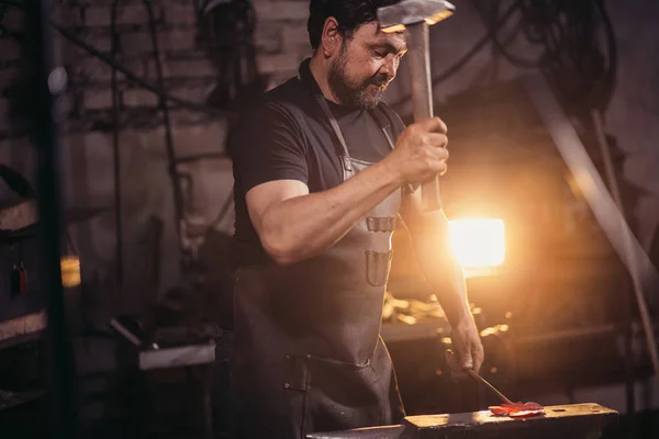 Herrero trabajando metal con martillo en yunque en la forja —  Fotos de Stock