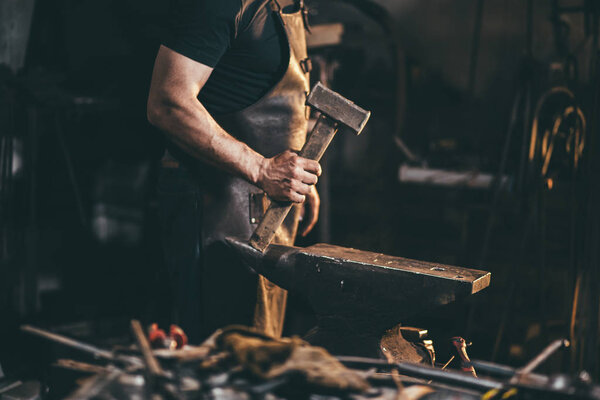 Blacksmith working on metal on anvil at forge