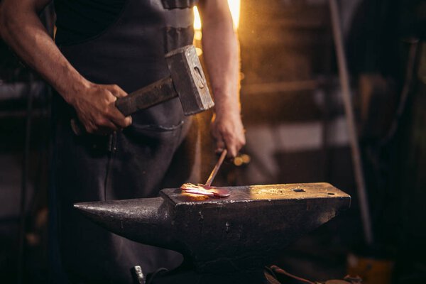 blacksmith manually forging molten metal on anvil in smithy workshop