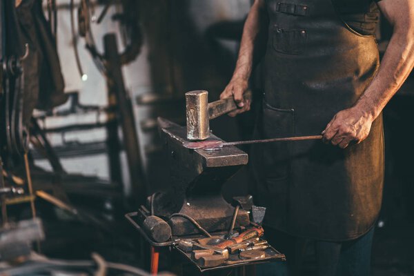 blacksmith manually forging the molten metal on the anvil in smithy