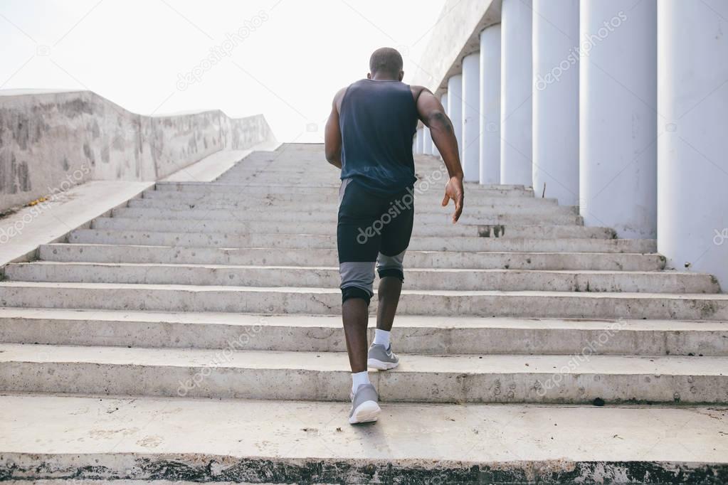 man african running up flight of stairs, training outdoor while jogging up steps