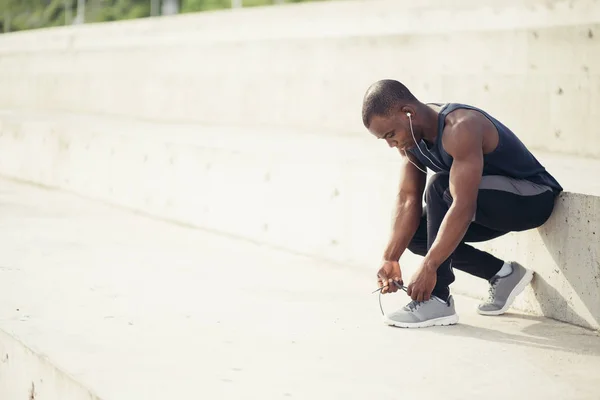 African male runner tying his shoe on steps — Stock Photo, Image