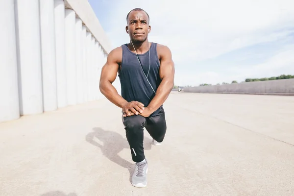 Runner in black sportswear stretching legs before doing morning workout — Stock Photo, Image